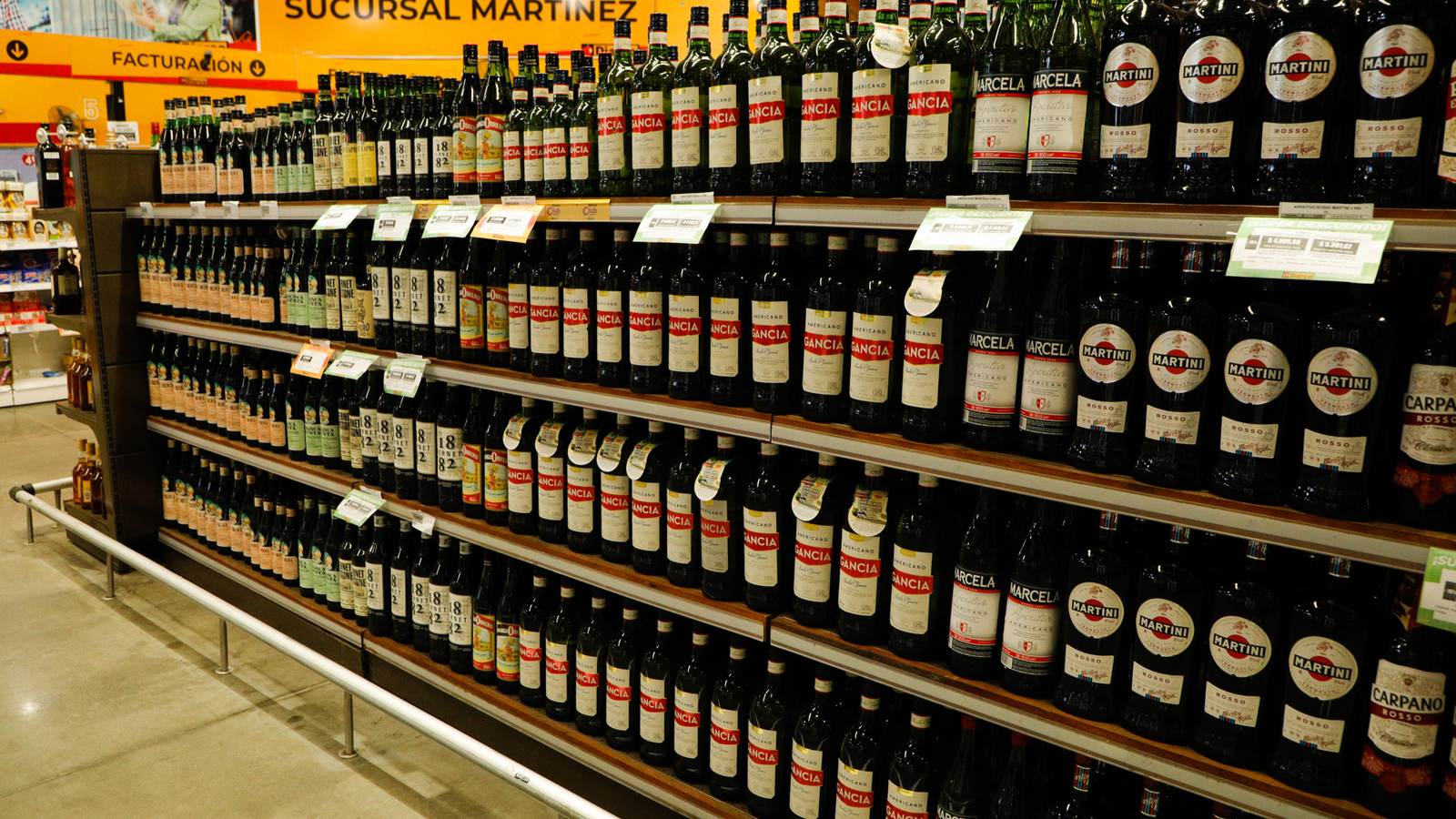 Pasillo de supermercado con góndolas de bebidas en perspectiva, con sus etiquetas de precio y material de punto de venta.